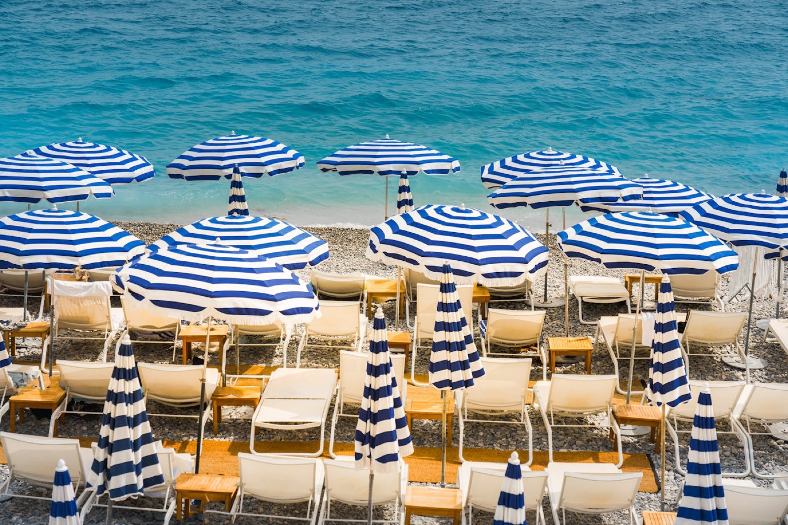 Plage privée La Jetée Juan-les-Pins — rangée de parasols rayés bleus et blancs, transats en bois clair, mer Méditerranée