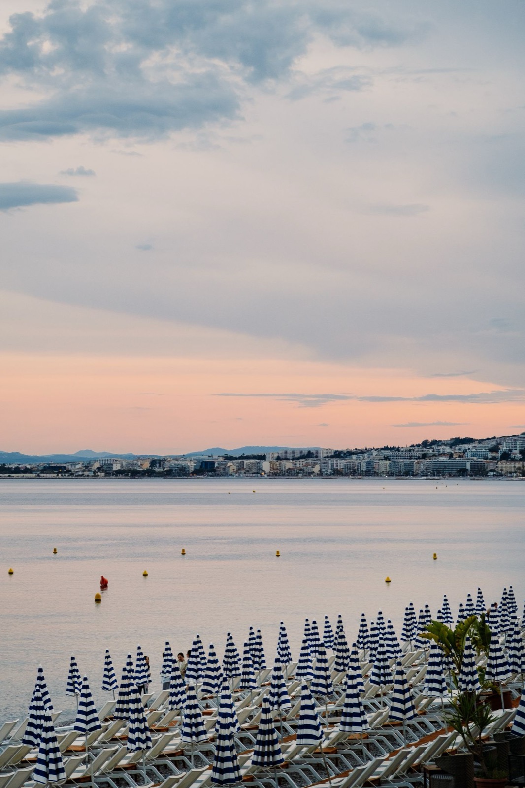 Coucher de soleil sur la baie de Juan-les-Pins — vue depuis la plage La Jetée vers le Cap d'Antibes, parasols rayés bleus