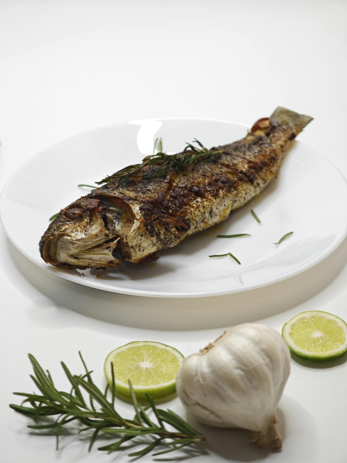 Poisson entier grillé au feu de bois — signature seafood La Jetée Juan-les-Pins, romarin, ail confit et citron vert